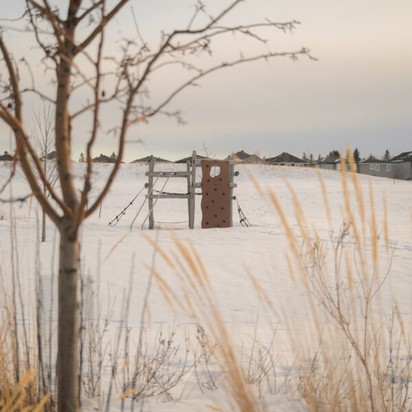 Snow covered playground structure seen through tall grasses in Trumpeter by Big Lake, Edmonton, Alberta.